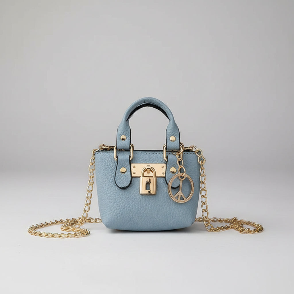 A light blue pebbled leather mini handbag with a gold chain strap and gold padlock clasp, held by a hand with red nail polish over a white textured fabric background.