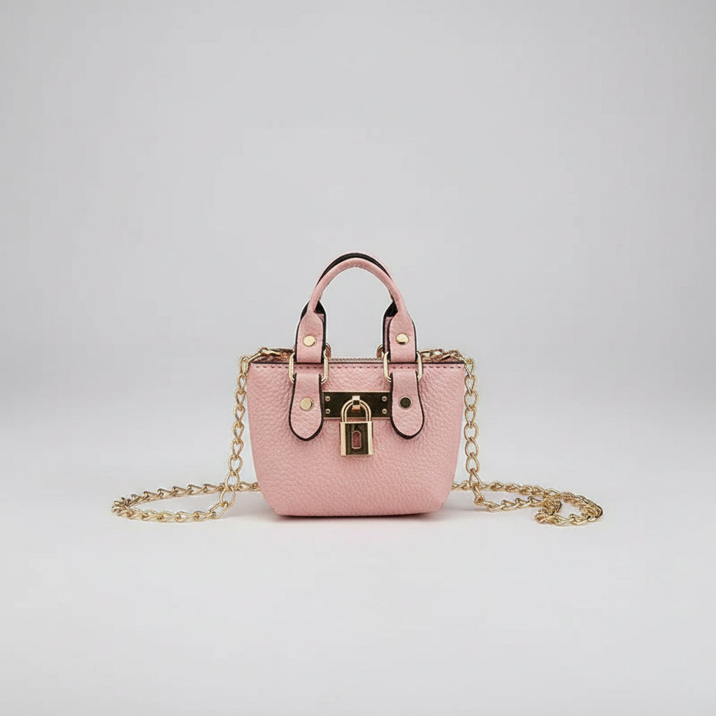 Pink handbag with gold chain and lock held by a hand against a light background
